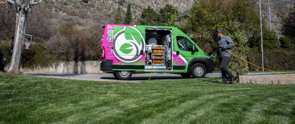 A van with hose and a person spraying a lawn in South Jordan, UT.